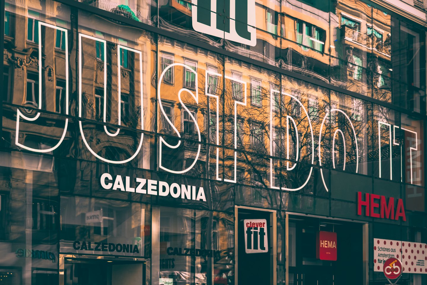 Szyldy sklepów detalicznych odbijające się w nowoczesnej fasadzie szklanego budynku.
