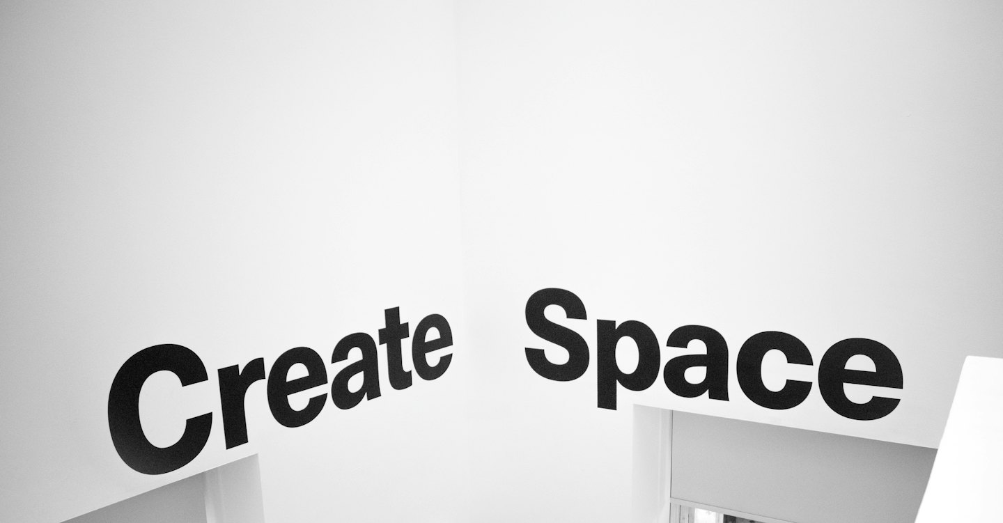 Czarny napis Create Space na białej ścianie.